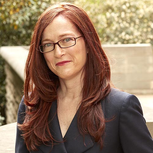 A woman with red hair and glasses is posing for a photo.